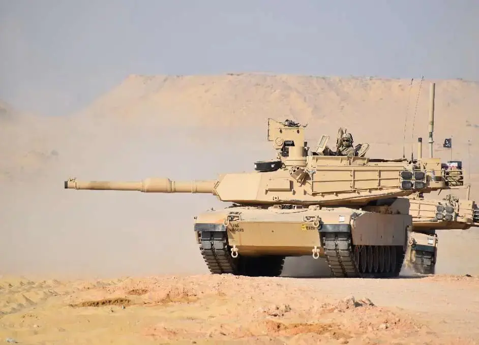 A tank driving down the road near some sand.