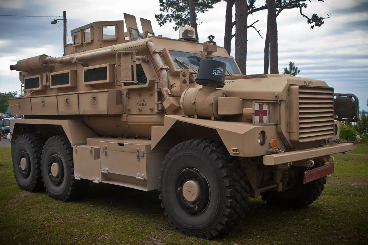 A military vehicle parked in the grass near trees.