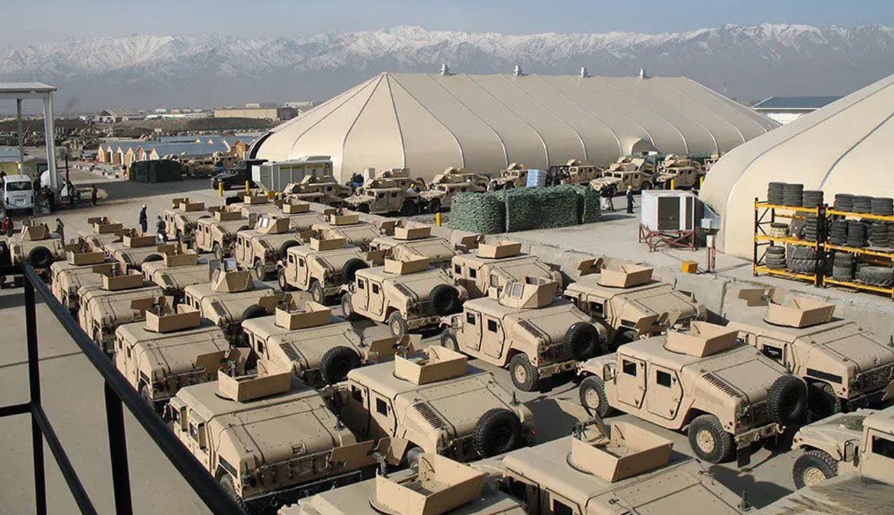 A large group of military vehicles parked in front of tents.