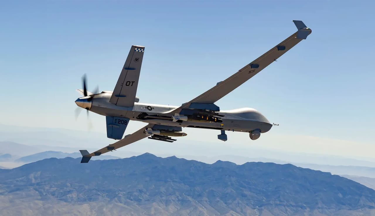 A military aircraft flying in the sky over mountains.